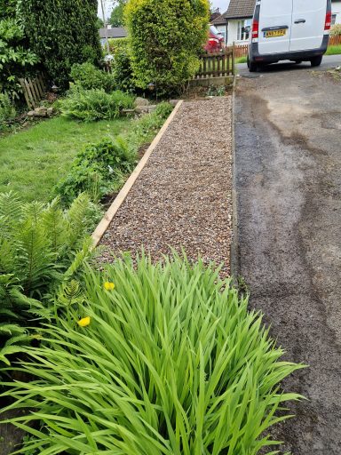 Gravel path alongside lush green plants and a parked van.