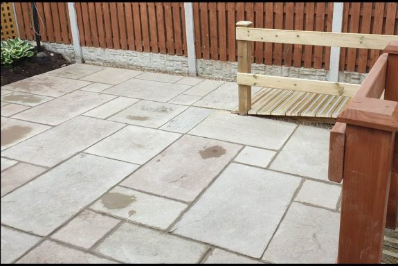 Paved garden patio with wooden wheelchair ramp and fence in the background.