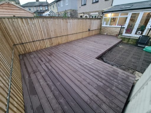 Wooden decking area enclosed by a wooden fence, with brown composite decking and house in the background.