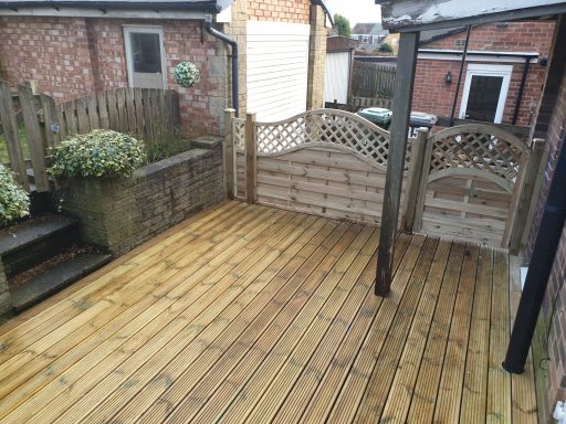 Wooden decking area with steps and omega fence panels and matching gate in a garden setting.