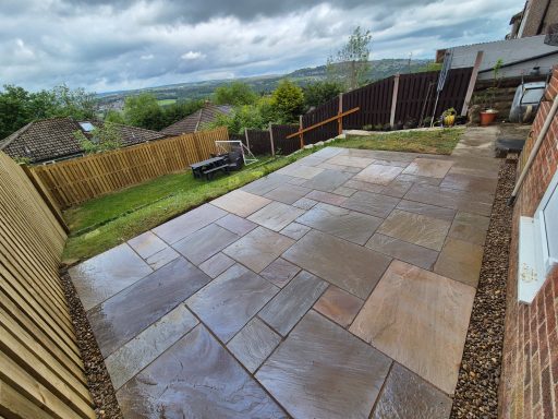 A newly paved patio area with a lawn and wooden fence in the background.