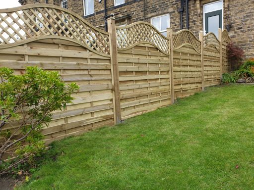 Wooden fence with curved trellis topping, beside a green lawn and brick house.