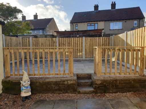 Enclosed garden area with wooden fencing, steps, and a gnome statue in front.