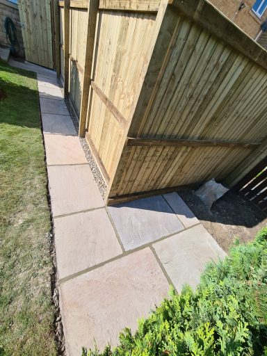 Paved pathway alongside wooden fencing in a garden setting.