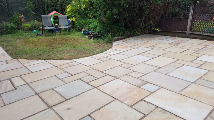 Patio with stone paving, grassy area, and a children's playhouse in the background.