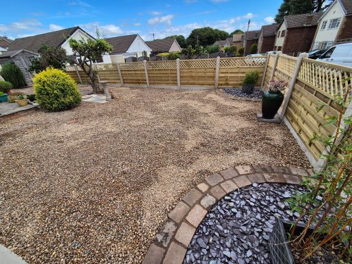 A gravel garden with a few plants and a wooden fence in a residential area.