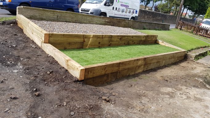 Raised wooden platform with gravel and grass areas, set in a landscaped environment.