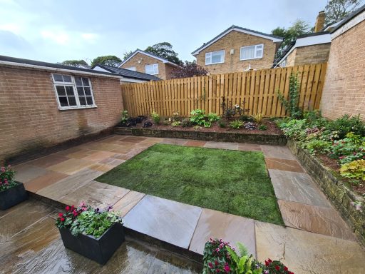 A landscaped garden with stone patio, grass area, and flower planters under cloudy skies.